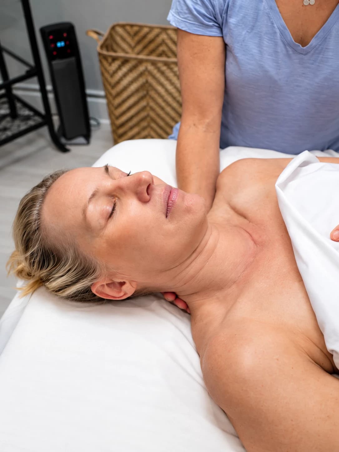 A client resting with her eyes closed while her therapist works along her shoulder
